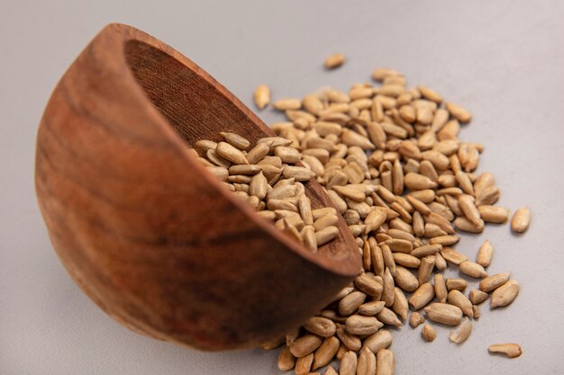 Side view of organic shelled sunflower seeds falling out of a wooden bowl on a grey wall