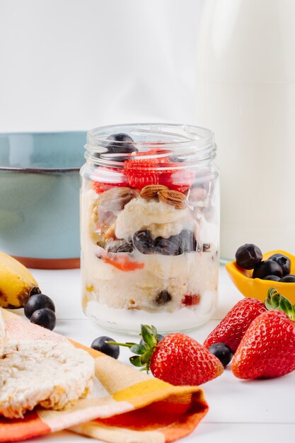 Side view of overnight oats with fresh strawberries blueberries and nuts in a glass jar on rustic surface