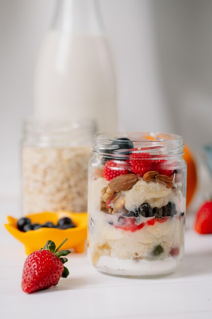 Side view of overnight oats with fresh strawberries blueberries and nuts in a glass jar on rustic table