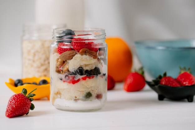 Side view of overnight oats with fresh strawberries blueberries and nuts in a glass jar on rustic table