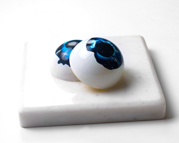 Free photo side view painted blue eyes in the form chocolate sweets on white stand