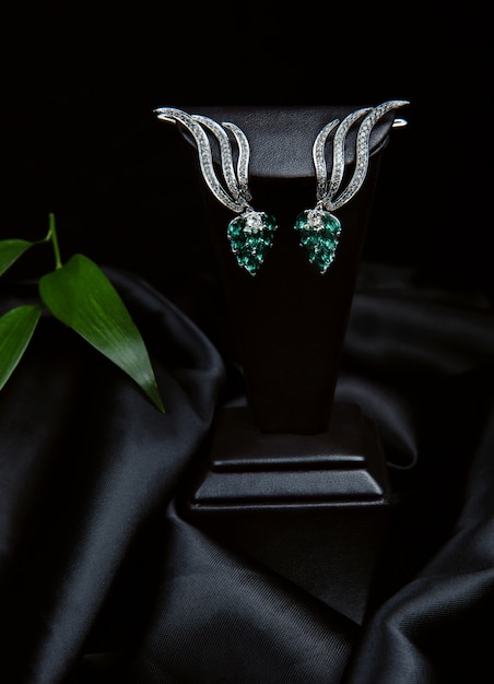 Free photo side view of a pair of silver diamond earrings with emerald on black wall on black