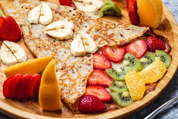 Side view pancake crepes with banana strawberry kiwi and orange on a plate