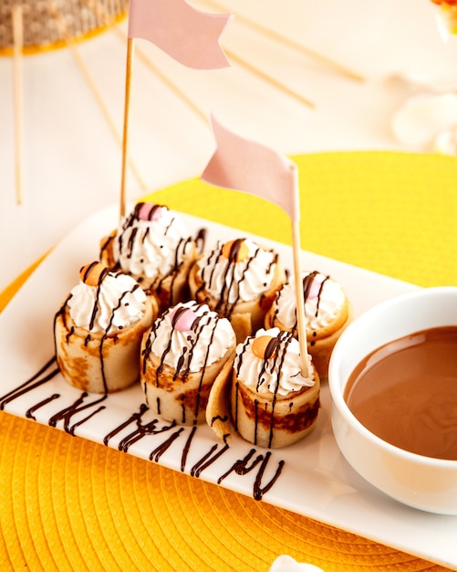 Side view of pancake rolls with whipped cream and chocolate on yellow