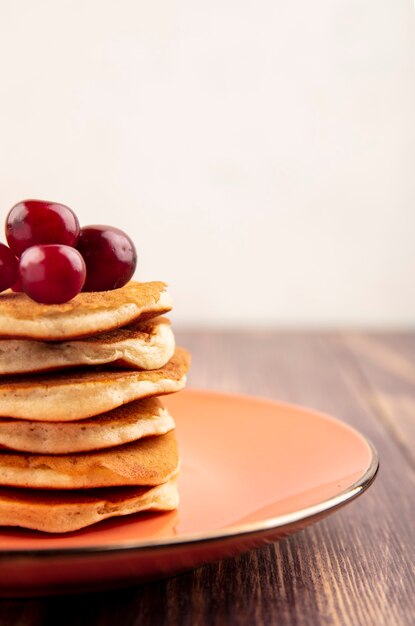 Side view of pancakes with cherries in plate on wooden surface and white background