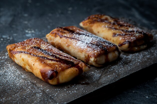 Side view pancakes with chocolate syrup and powdered sugar in cutting board