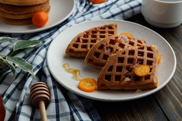 Side view of pancakes with kumquat slices in plate on wooden background