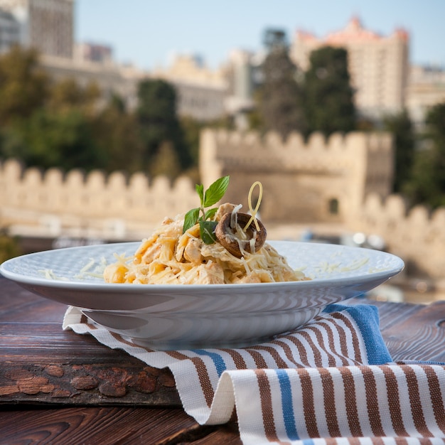 Side view pasta with cheese and mushrooms in a white plate on a dark wooden table with city view