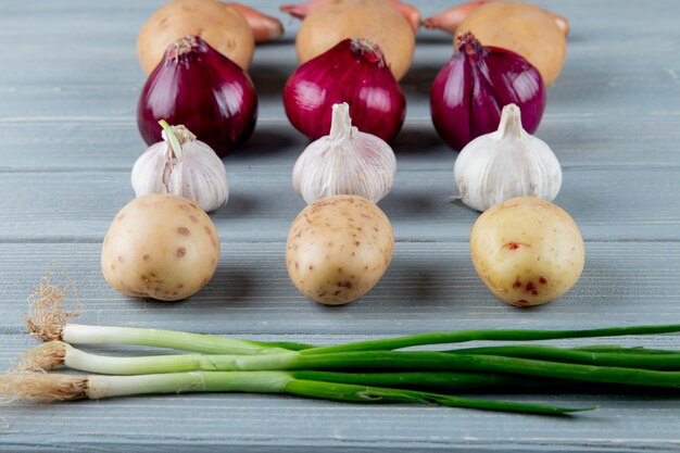 Side view of pattern of vegetables as potato onion garlic scallion on wooden background