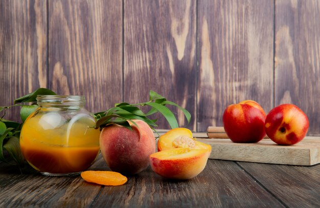 Side view of peach jam in a glass jar and fresh ripe peaches on wooden background