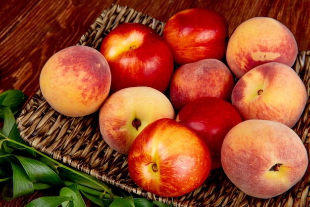 Side view of peaches in basket plate on wooden table decorated with leaves