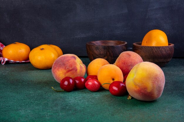 Side view peaches with apricots and cherries and tangerines in a bowl