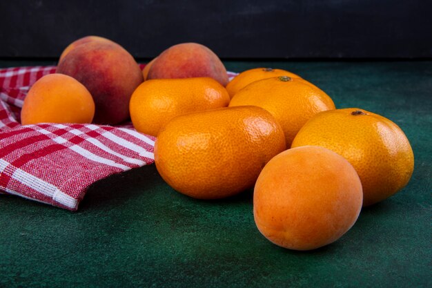 Side view peaches with tangerines and apricots on kitchen towel