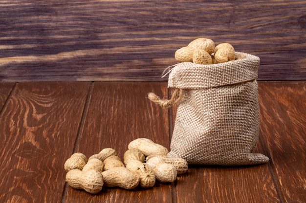 Free photo side view peanuts in shell in a bag and on a wooden table