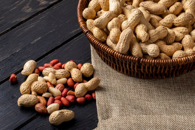 side view peanuts in shell in a basket with peeled on a black wooden table