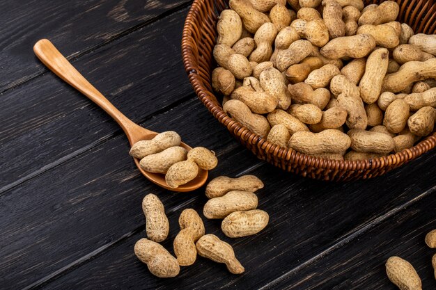 Side view peanuts in shell in a basket and in a wooden spoon on a black wooden table