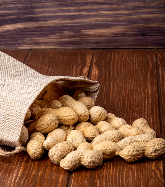 Free photo side view peanuts in shell from a bag on a wooden table