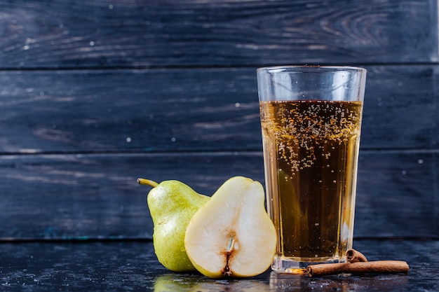 Side view of pear lemonade in a glass with fresh pear halves at black wooden background