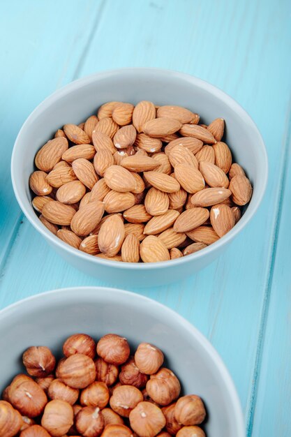 Side view of peeled almond and hazelnuts in bowls on blue background