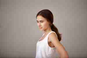 Free photo side view of pensive thoughtful young twenty year old woman dressed in white top posing isolated at blank copyspace wall, looking down, daydreaming, having deep in thoughts expression