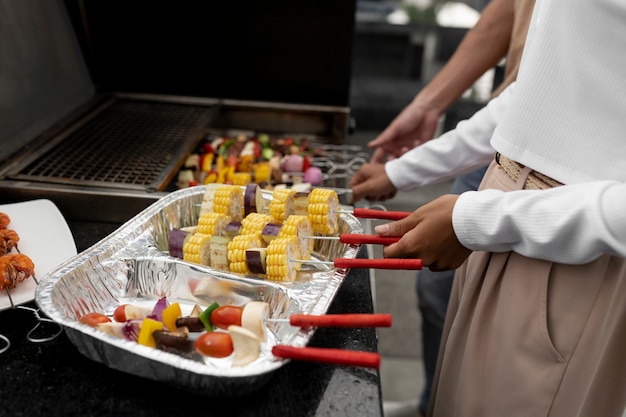 Side view people putting skewers on grill