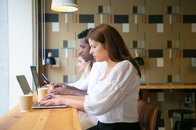 Side view of people working on laptops and sitting at table near window