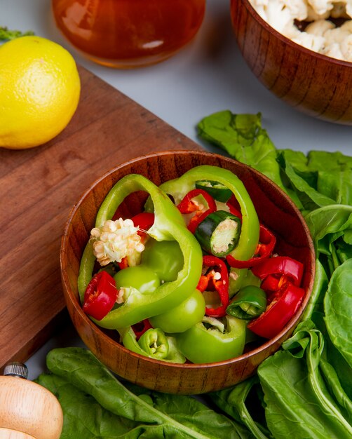 Side view of pepper slices in bowl with spinach melted butter cauliflower and lemon on cutting board on blue background