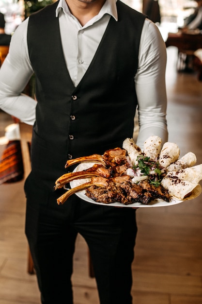 Side view of a person holding a plate with different types of kebab on