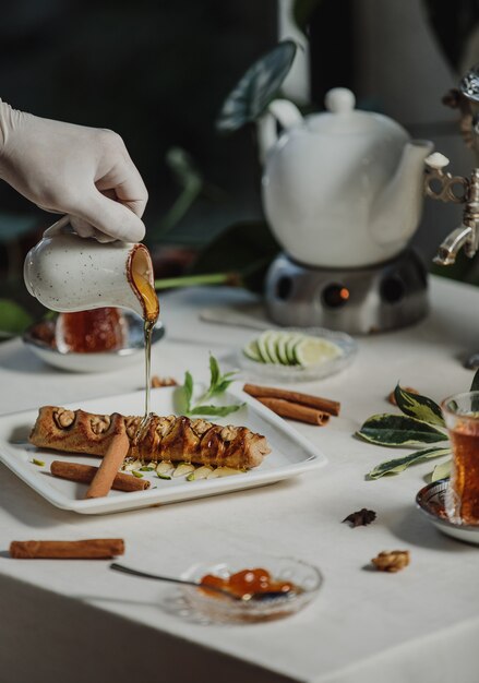 Side view of a person pouring honey on biscuit roll filled with walnuts on a table