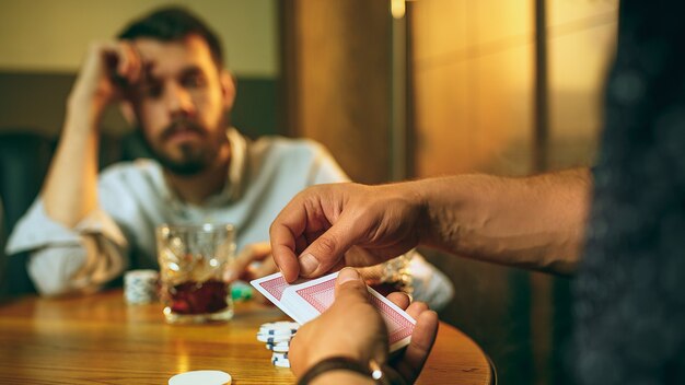 Side view photo of friends sitting at wooden table. Friends having fun while playing board game.