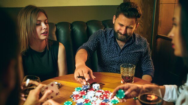 Free photo side view photo of friends sitting at wooden table. friends having fun while playing board game.