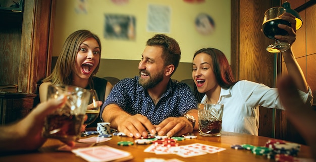 Free photo side view photo of friends sitting at wooden table. friends having fun while playing board game.