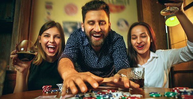 Side view photo of friends sitting at wooden table. Friends having fun while playing board game.