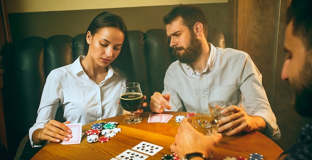 Side view photo of friends sitting at wooden table. Friends having fun while playing board game.