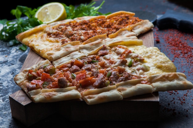 Side view pide with pieces of meat and parsley and lemon and pizza knife in cutting board