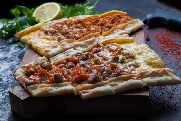 Side view pide with pieces of meat and parsley and lemon and pizza knife in cutting board