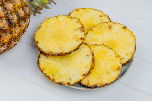 Side view of pineapple slices in plate with whole one on wooden background