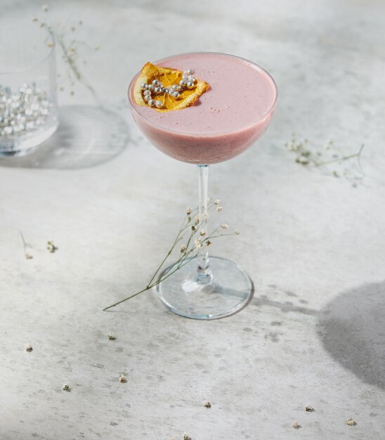 Side view of pink fruit cocktail decorated with dried orange slice in a glass on white wall