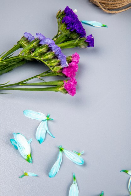 Side view of pink and purple statice flowers with flower petals scattered on white table