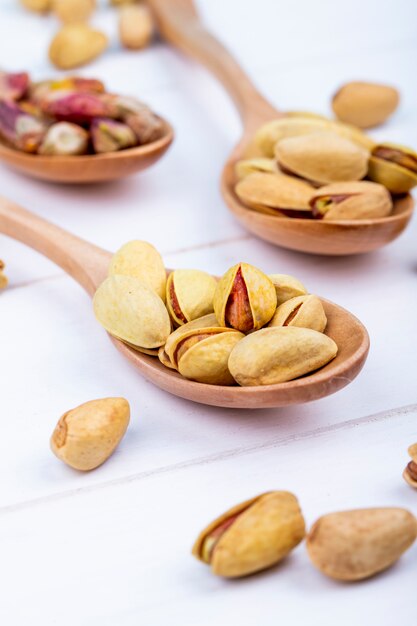 Side view of pistachio nuts on a wooden spoon on white background