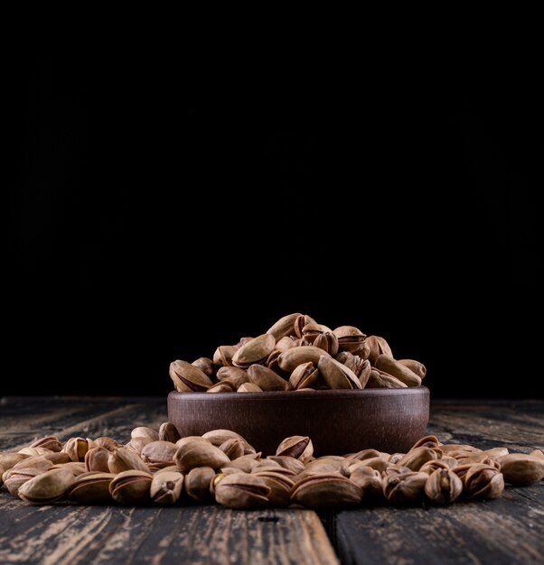 Side view pistachios in a bowl on dark