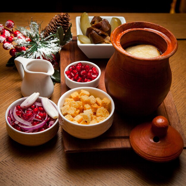 Side view piti with crackers and pomegranate seeds and pickles in clay jug on wooden table