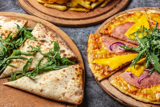 Foto gratuita vista laterale pizza prosciutto e formaggio pizza con cipolla rossa e formaggio fuso pizza calzone con rucola sul tavolo