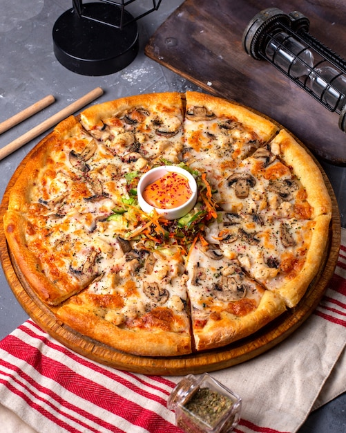 Side view of pizza with chicken and mushrooms served with sauce and vegetables salad on wooden plate