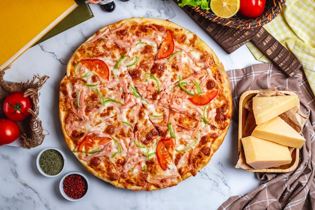 Side view of pizza with green peppers tomatoes ham and cheese on a wooden plate on the table