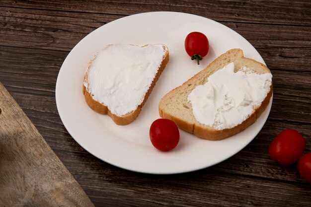 Side view of plate of bread slices smeared with cottage cheese and tomatoes on wooden background