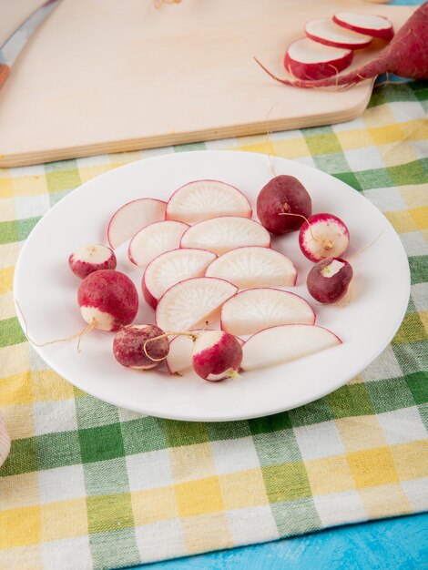 Side view of plate full of whole and sliced radish on plaid cloth surface