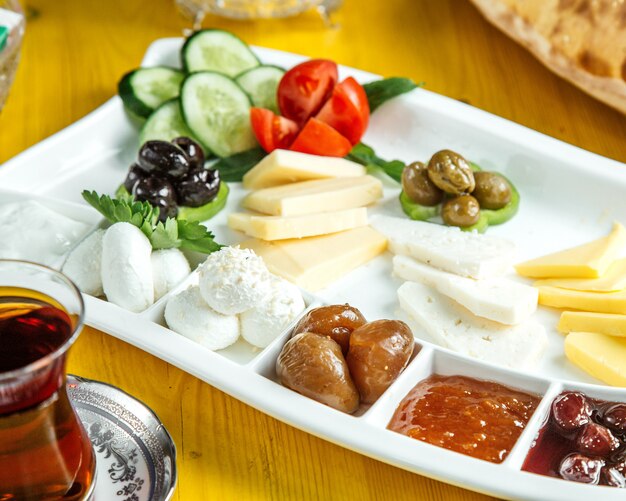 Side view of a plate with breakfast food with fresh vegetables olives cheese honey and jam served with tea