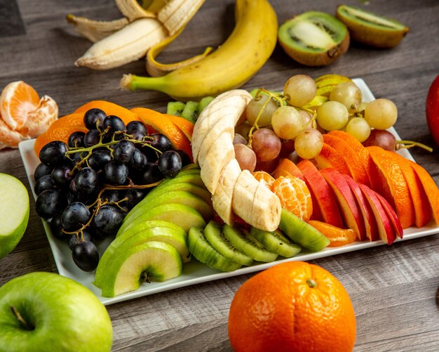 Вид сбоку тарелка с нарезанными фруктами банан, виноград, яблоко, киви, апельсин