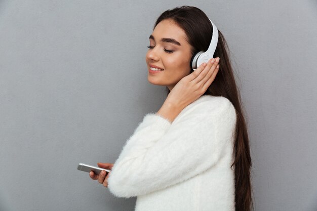 Side view of pleased brunette woman in sweater and headphones